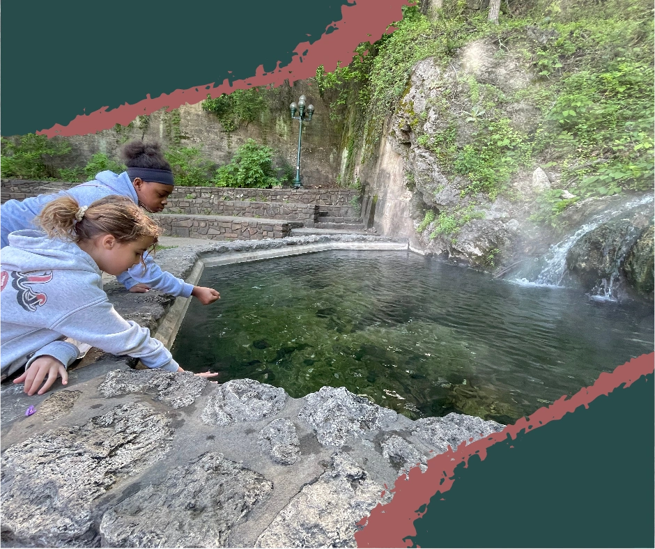 Two kids touching the thermal water flowing from a hot spring fountain at Hot Springs National Park, Arkansas, near historic Bathhouse Row.